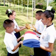 Skolebørn fra Escuela Central San Sebastián i Costa Rica er ved at hejse et flag, som repræsenterer mål 12: Ansvarligt Forbrug og Produktion.